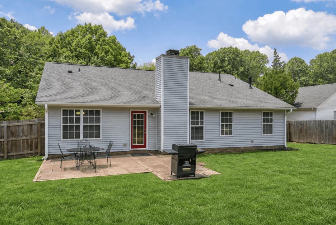 Fenced back yard with a patio dining set and grill behind a CFR rental home